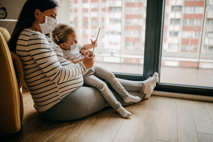 Pregnant woman with mask reading to daughter